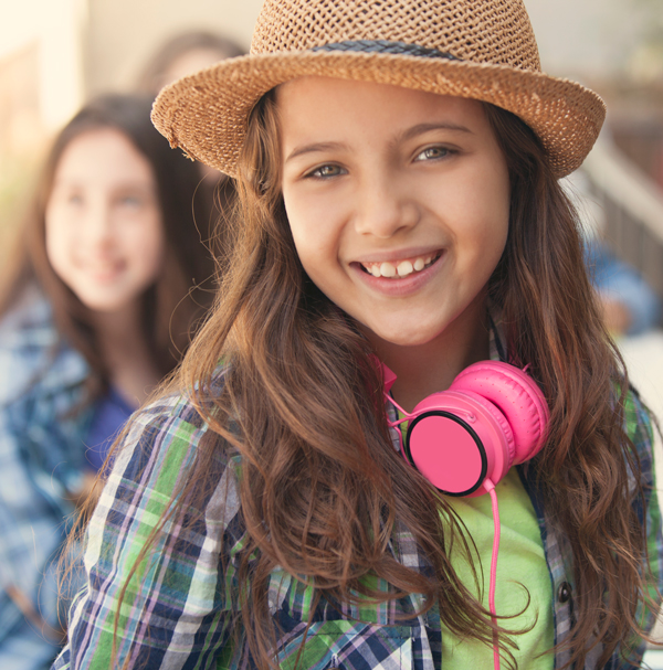 Young girl smiling with pink headphones around her neck.
